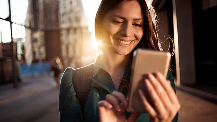 UX verhindert Frustration und schafft positive Nutzungserlebnisse In der Ausbildung zum UX Designer positive Nutzererlebnisse schaffen: Lächelnde Frau am Smartphone