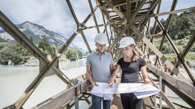 Bachelorstudium Bauingenieurwesen Angehende Bauingenieurin und Bauingenieur der Fachhochschule Graubünden mit Plänen in den Händen auf einer Brücke.