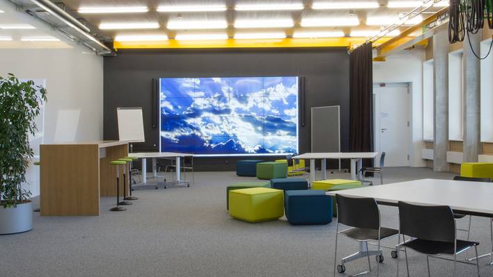 Service Innovation Lab (SIL) Ein grosser Raum mit Sitzgelegenheiten und grossem Bildschirm im Hintergrund